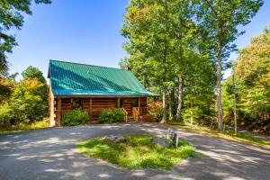 une cabane en rondins avec un toit vert et une allée. dans l'établissement Pet-friendly Rustic Cabin with Game Room and Deck, à Pigeon Forge