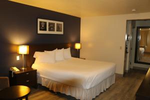 a hotel room with a bed with white sheets and pillows at Empire Inn & Suites in Red Deer