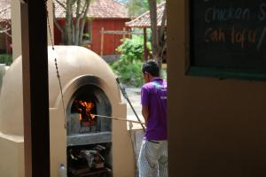 a man is standing next to a pizza oven at Biru Meno Beach Bungalows in Gili Meno