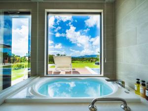 eine Badewanne im Bad mit einem großen Fenster in der Unterkunft Kanehide Kise Country Club in Nago