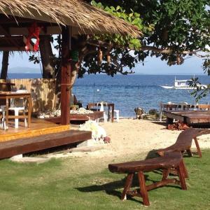 Liwayway sa Bohol Pamilacan Resort في Baclayon: شاطئ مع مقاعد وطاولات والمحيط