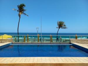a swimming pool next to the beach with palm trees at Studio Lateral Vista Mar Barra Apartamento Inteiro Completo in Salvador