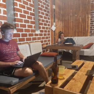 a man sitting on a bench with a laptop at Wally's House Mancora in Máncora