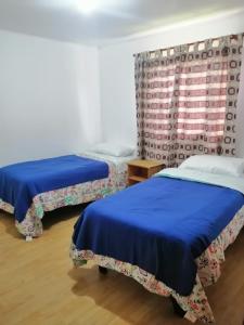 a room with two beds with blue sheets and a window at Alojamiento Freire - Caviahue in Freire
