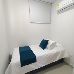 a white room with a bed with blue and white pillows at Samaria - Apartamento en Club de Playa, Santa Marta in Santa Marta