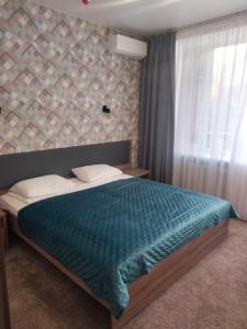 a bedroom with a bed with a blue blanket and a window at Hotel Prydesnyansky in Chernihiv