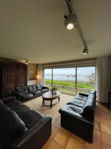 a living room with black leather couches and a large window at Vacances paradisiaques au coeur de l'Ile de Bréhat in Bréhat