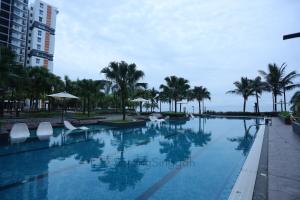 a swimming pool with white chairs and palm trees at SarangSinggah@Timurbay Seafront in Kuantan