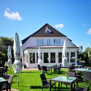 eine Gruppe von Tischen und Sonnenschirmen vor einem Gebäude in der Unterkunft Fitschen am Dorfteich in Wenningstedt-Braderup