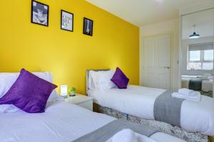 two beds in a room with yellow walls and purple pillows at Honeysuckle Road in Sheffield