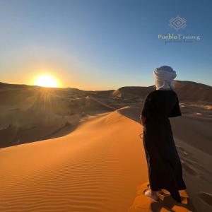 a woman standing on a sand dune in the desert at Pueblo Touareg - Private Tents in Merzouga