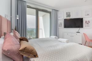 sypialnia z białym łóżkiem z poduszkami i telewizorem w obiekcie Apartments Mazowiecka Pobierowo by Noclegi Renters w Pobierowie
