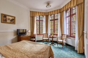 a bedroom with a bed and a desk and windows at Spa Hotel Villa Ritter in Karlovy Vary