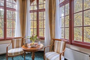 a room with a table and chairs and windows at Spa Hotel Villa Ritter in Karlovy Vary