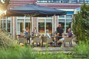 a group of people sitting at tables under an umbrella at Hotel Molenbos Texel in De Cocksdorp