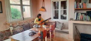 a woman sitting on a couch playing a guitar in a living room at Maison d'Hôtes Irocha in Tisseldeï