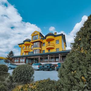 a yellow building with cars parked in a parking lot at Motel Almy in Zenica