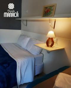 a bed in a small room with a lamp on a table at Pousada Manacá in Piraju