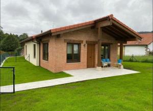 een klein bakstenen huis met een patio en gras bij BUNGALOW LA COCINA in Valdaliga 