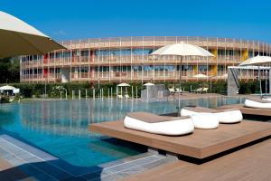 una piscina con bancos y sombrillas frente a un edificio en Isola di Albarella Hotel Capo Nord, en Isola Albarella