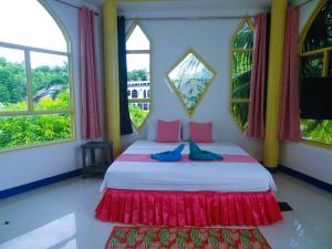 a bedroom with a bed with red and pink pillows and windows at MG Chateau Resort in El Nido