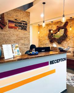 a man sitting at a reception counter in a restaurant at Harbour Komodo Hotel in Labuan Bajo