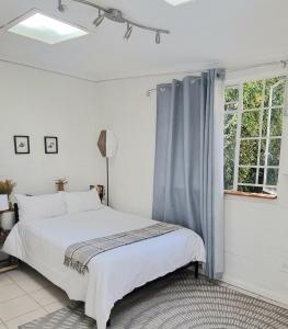 a white bedroom with a bed and a window at Sunlight Cottage in Cape Town