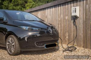 une voiture garée à côté d'une clôture avec une voiture électrique branchée dans l'établissement Hotel Molenbos Texel, à De Cocksdorp