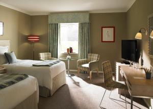 a bedroom with two beds and a desk and a television at The Goodwood Hotel in Chichester