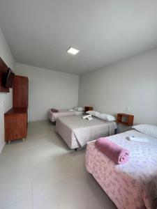 a room with three beds with pink sheets at Pousada Rosália in Penha