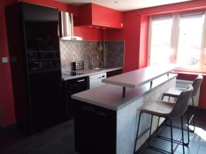 une cuisine avec des murs rouges et un comptoir avec des tabourets dans l'établissement Au Bercail, à Gérardmer