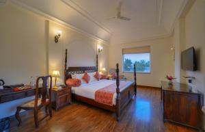 a bedroom with a bed and a desk and a television at WelcomHeritage Mount Valley Resort Ranthambore in Sawāi Mādhopur