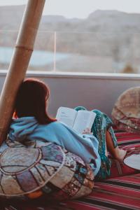 a girl laying on a bed reading a book at Nomads Hotel Petra in Wadi Musa