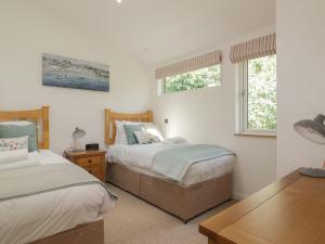 a bedroom with two beds and a table and two windows at 2 Faraway Fields in Liskeard