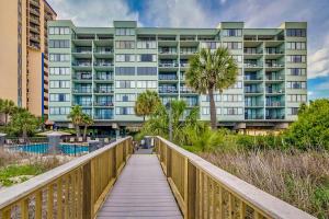 a wooden walkway leading to a building with palm trees at Carolina Dunes - 503 in Myrtle Beach
