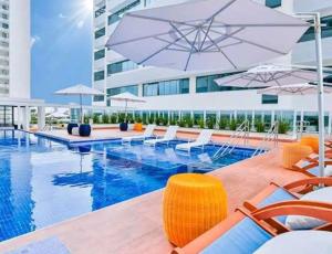 a pool with chairs and umbrellas next to a building at Flat Apart America Campos in Campos dos Goytacazes