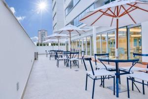 un patio esterno con tavoli, sedie e ombrelloni di Flat Apart America Campos a Campos dos Goytacazes