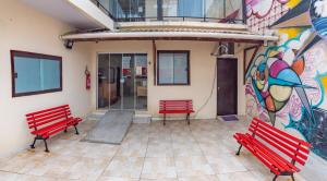 dos bancos rojos frente a un edificio con un mural en Dona Rosa Suites Privativas, en Arraial do Cabo