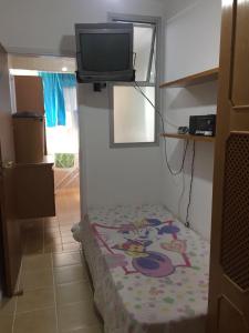 a small room with a bed and a tv on the wall at Apartamento Guaruja Pitangueiras in Guarujá