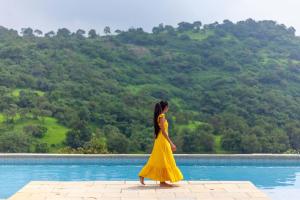 una mujer con un vestido amarillo caminando por una piscina en StayVista's Shivom Villa 12 - A Serene Escape with Views of the Valley and Lake, en Lonavala