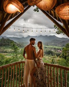a man and a woman standing on a balcony at Bird Hills Bamboo House in Karangasem