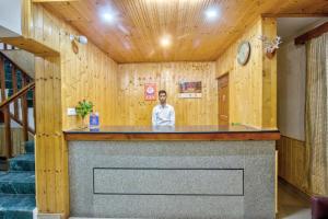 a man standing behind a counter in a room with wooden walls at Ayushman Hotels in Manāli