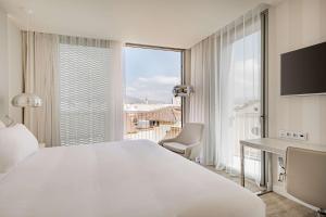 sypialnia z białym łóżkiem, biurkiem i oknem w obiekcie NH Málaga w Maladze