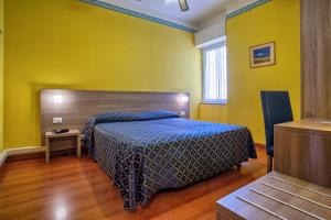 Schlafzimmer mit einem Bett mit blauer Tagesdecke und gelben Wänden in der Unterkunft Hotel Calypso in Ventimiglia