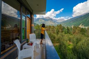 a person standing on a balcony looking out at the mountains at The 14 Gables, A Boutique Stay in Manāli