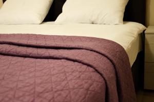 a bed with a purple blanket and white pillows at Hotel Leda in Sofia