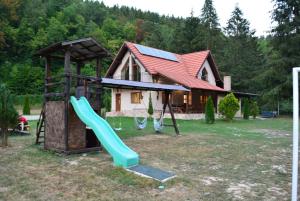 a playground with a slide and a house at cabana din padure in Finiş