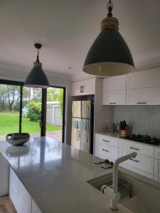 una cocina con armarios blancos y una isla de cocina con 2 luces en Jervis Bay Waters Edge Retreat - Access to Deep Water - Free late check out 2pm on Sundays, low season, en Woollamia