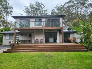 a house with a large deck with glass doors at Jervis Bay Waters Edge Retreat - Access to Deep Water - Free late check out 2pm on Sundays, low season in Woollamia