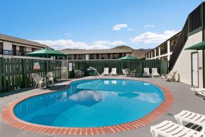 Travelodge by Wyndham Wenatchee في ويناتشي: وجود مسبح في الفندق مع الكراسي والمظلات